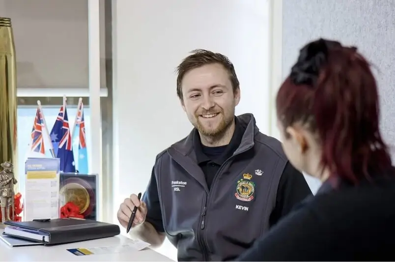 Two people talking at a desk and taking notes